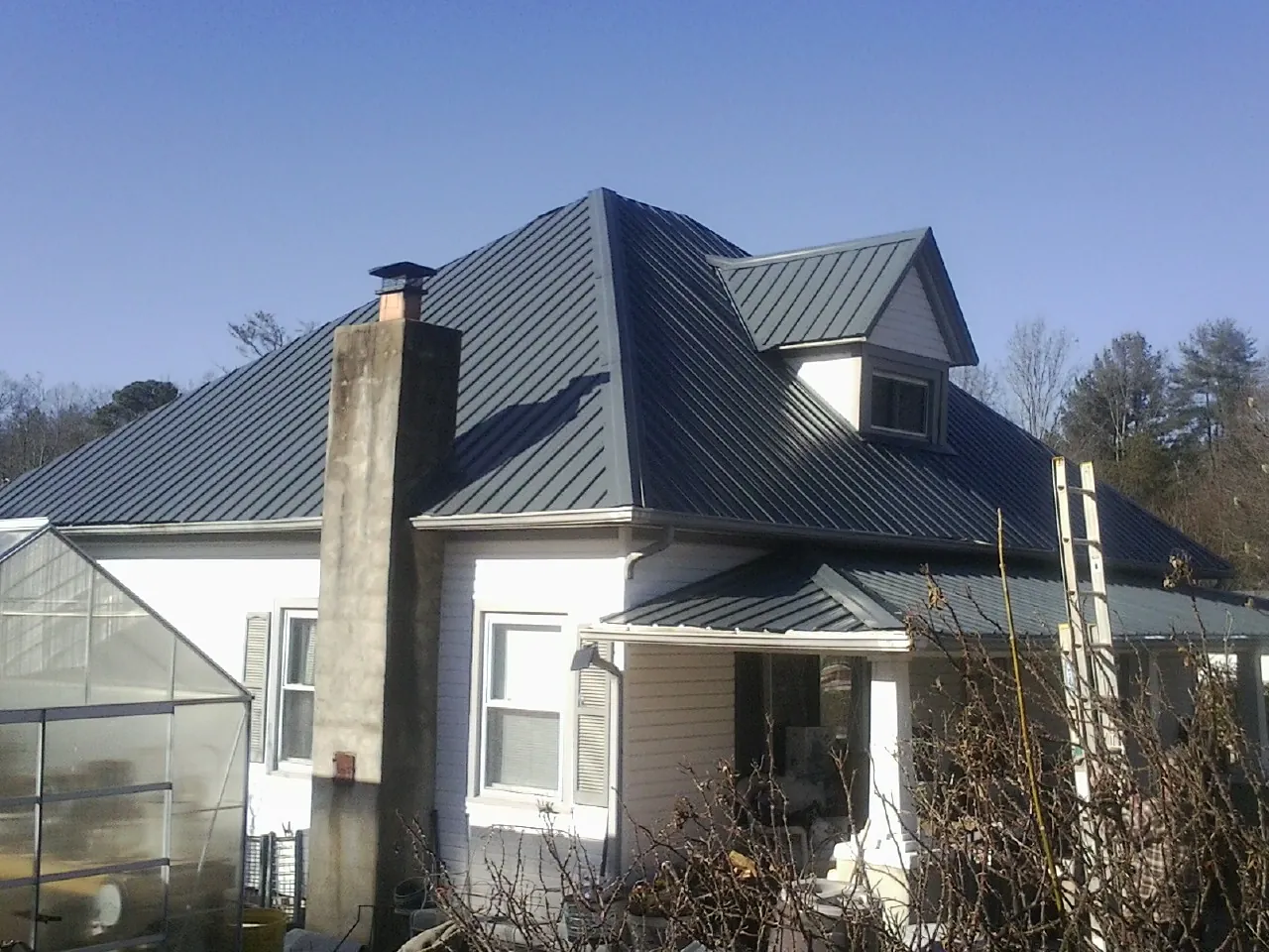 Dark blue standing seam metal roof on a white farmhouse with dormer — Slate & Tile Roof Repair by Roofing Brothers in Harrisville