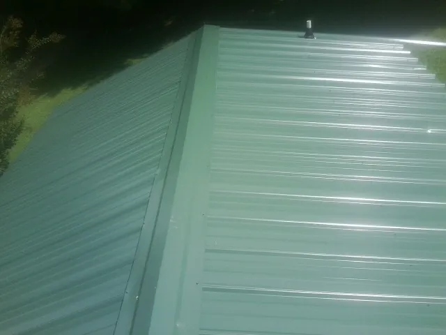 New green metal panels meeting at the ridge of a roof — Flat Roof Repair work by our crew in Harrisville